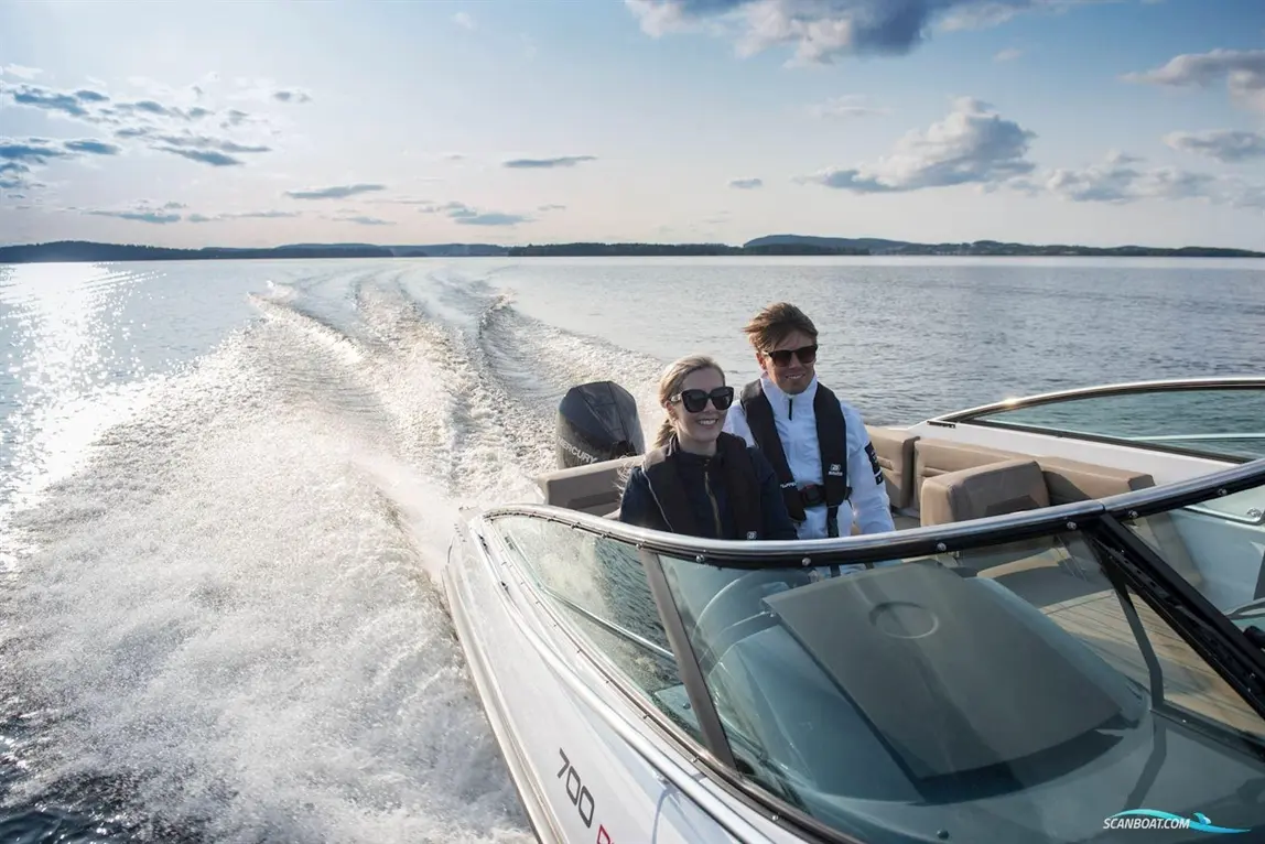 A man and woman enjoy a boat ride on a lake, with sunlight sparkling on the water and a distant shoreline visible.